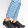 Black sneakers with gold accents worn by someone with blue jeans